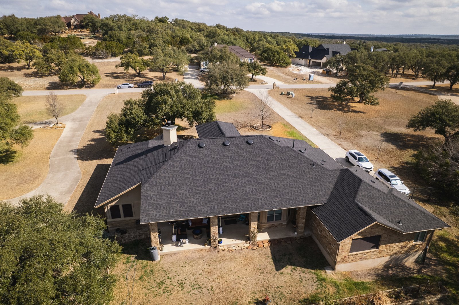 Completed dark shingle roof on a stone ranch home, aerial view