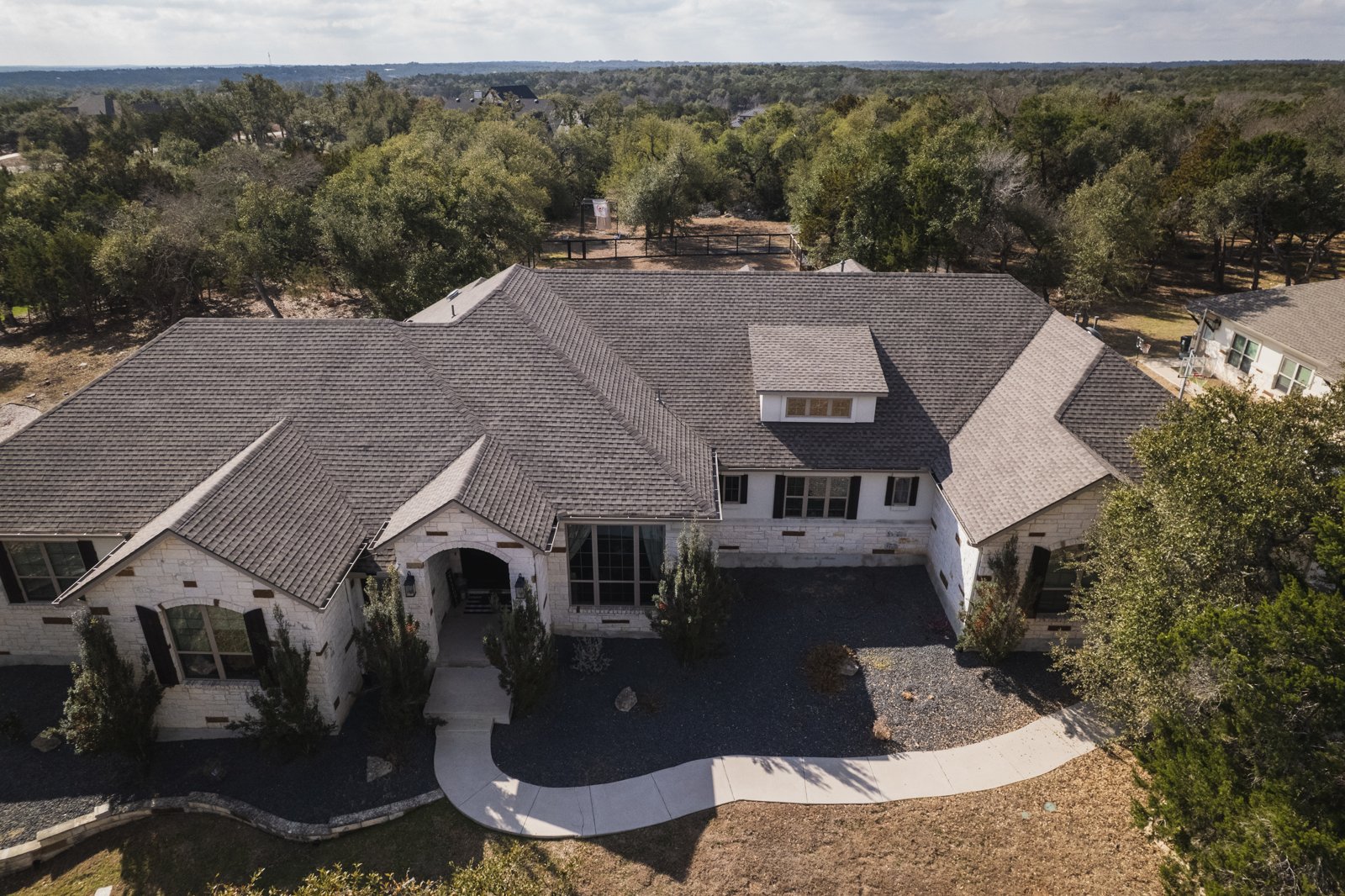 Aerial front view of a completed shingle roof on a white stone home
