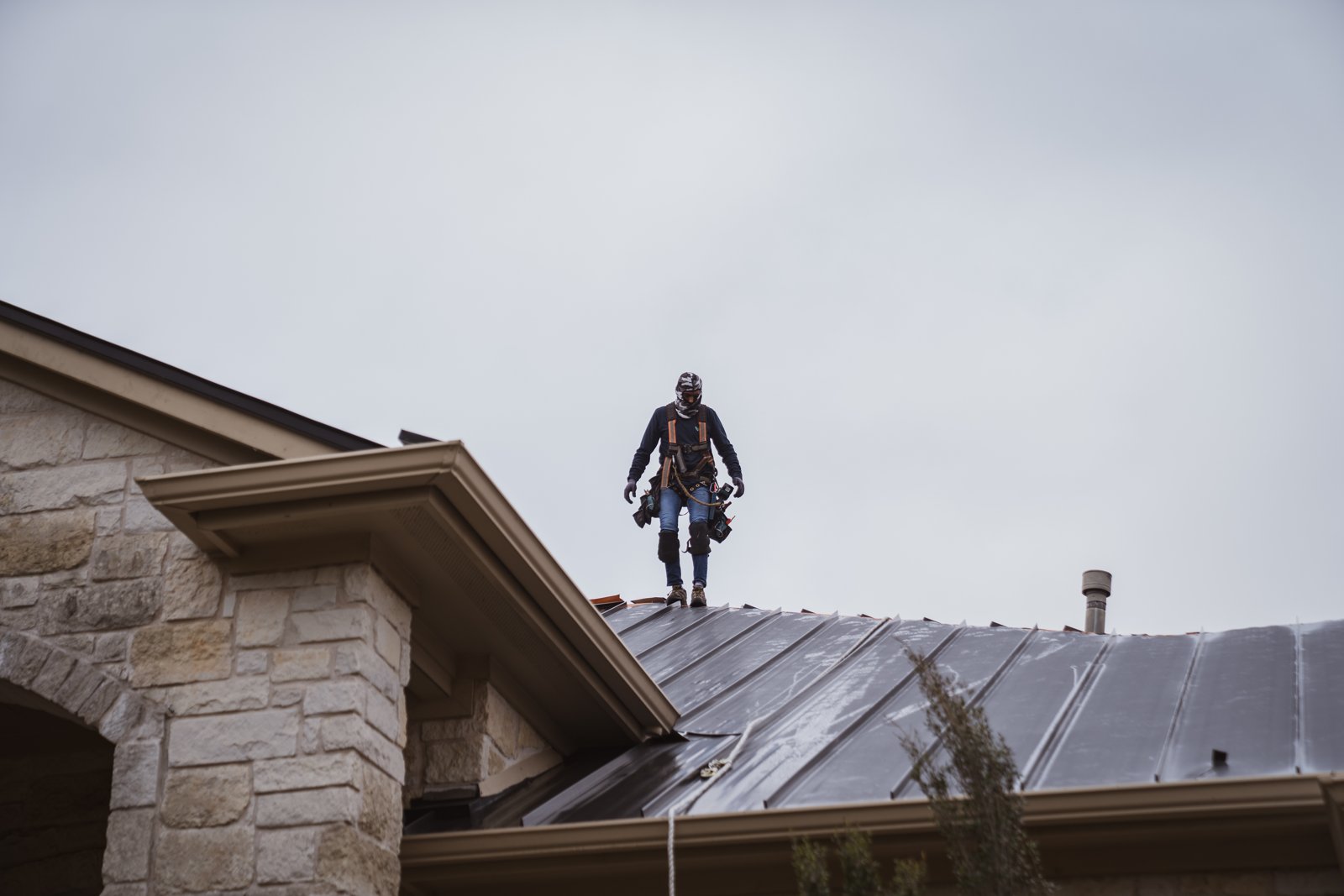 Hermes crew member walking the ridge of a new standing seam metal roof on a stone home, Driftwood, TX